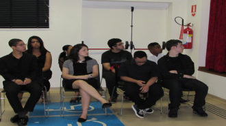 Foto de oito adolescentes do curso Laboratório de Imagem sentados em cadeiras pretas.