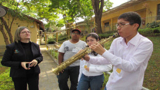 Foto de três usuários e uma técnica. Um dos usuários está tocando saxofone.