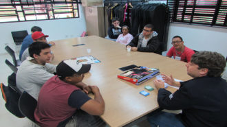 Foto da sala de aula. Oito usuários e um técnico sentados próximos a uma mesa. Os usuários estão jogando um jogo de tabuleiro.