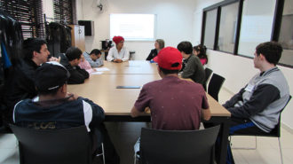 Foto da sala de aula. Dez usuários e uma técnica sentados próximos a uma mesa, conversando.