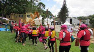 Foto de competidoras passando pelo corredor de remadoras rosas.
