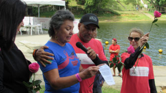 Foto de uma das remadoras falando ao microfone e sendo abraçada por um dos organizadores do evento.
