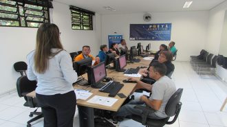 Foto da sala de aula. 9 usuários sentados em frente aos computares e uma técnica em pé na sala de aula.