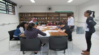 Foto da sala de artes. Oito usuários próximos à mesa, desenhando em folhas brancas. Duas técnicas em pé, acompanham a atividade.