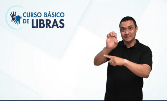 Imagem colorida. Um homem fazendo sinal em Libras e no canto superior um sinal em Libras e o texto curso básico de Libras.