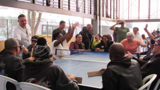 Imagem colorida da quadra do SRLMH. Pessoas jogando Takkyu Volley.