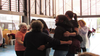 Imagem colorida da quadra do SRLMH. Mulheres se abraçando.