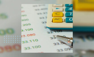Fotomontagem colorida. A parte inferior de uma calculadora por cima de uma folha com diversos números. No canto inferior, uma caneta.
